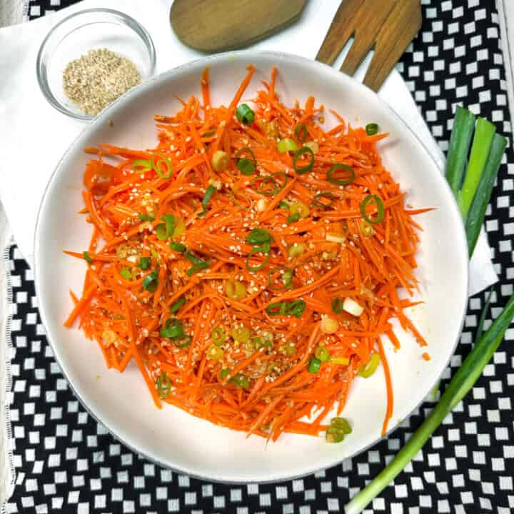 Ginger carrot slaw in a serving bowl topped with chopped scallions and sesame seeds.