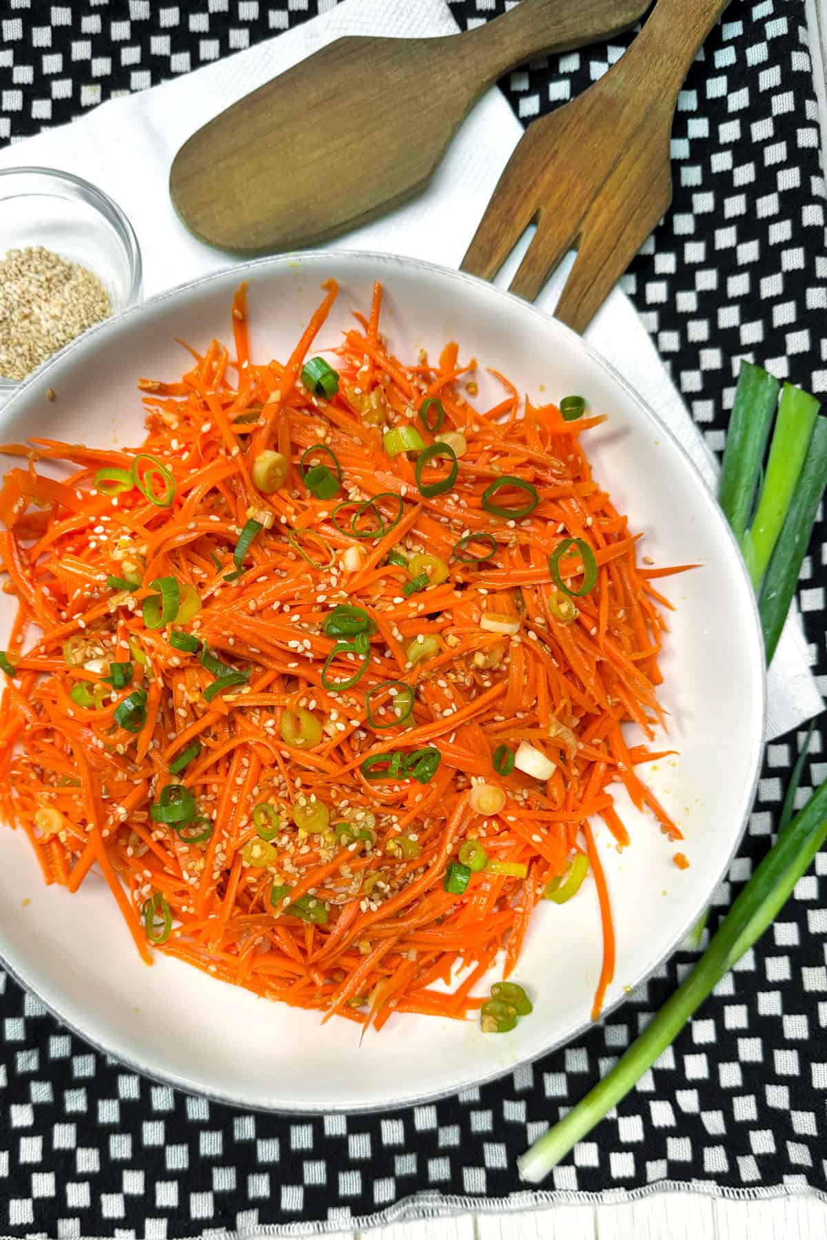 Ginger carrot slaw in a serving bowl topped with chopped scallions and sesame seeds.