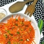 Ginger carrot slaw in a serving bowl with wooden serving utensils.