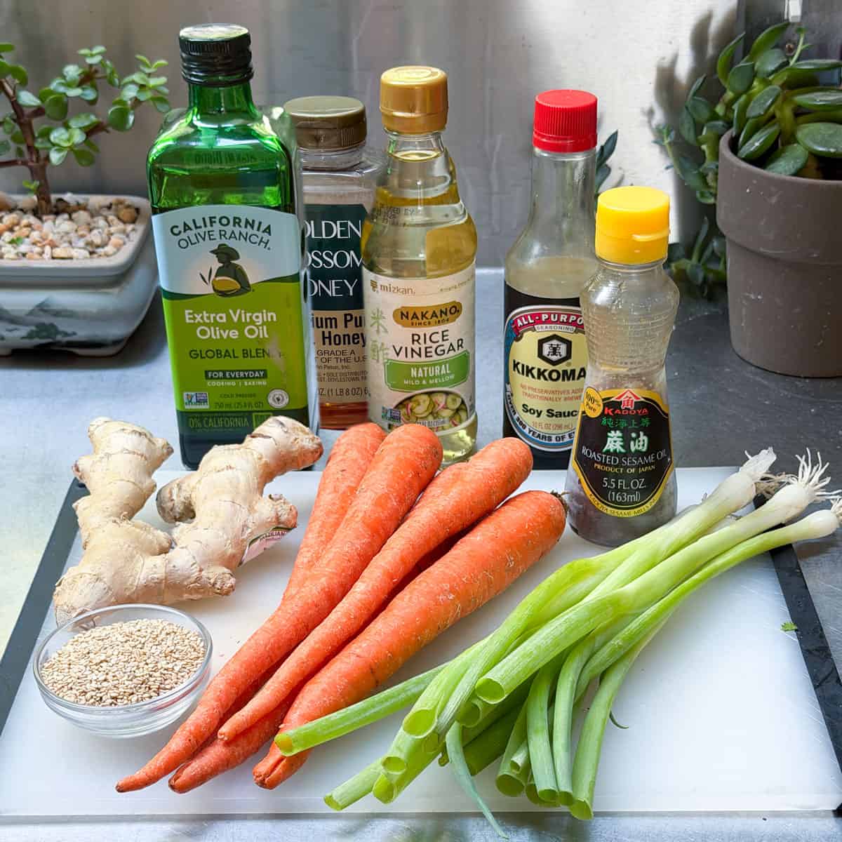 ingredients for ginger carrot slaw: bottles of olive oil, honey, vinegar, soy sauce and sesame oil; ginger root, carrots, scallions and sesame seeds.