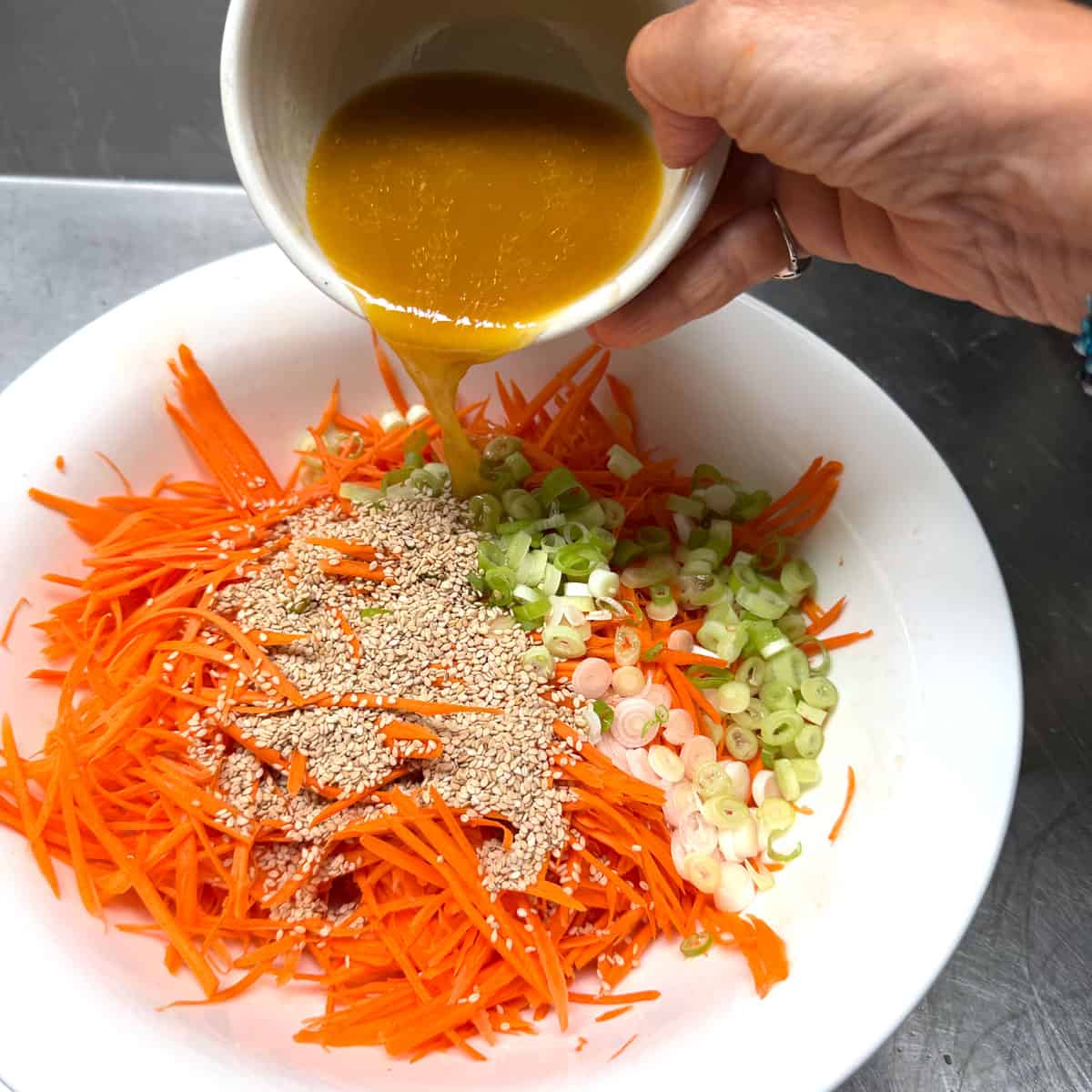 pouring ginger dressing over carrot slaw ingredients