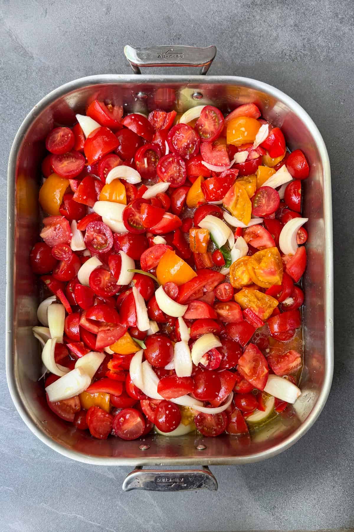 chunks of fresh tomatoes in a stainless steel roasting pan with onions, peppers, garlic and olive oil.