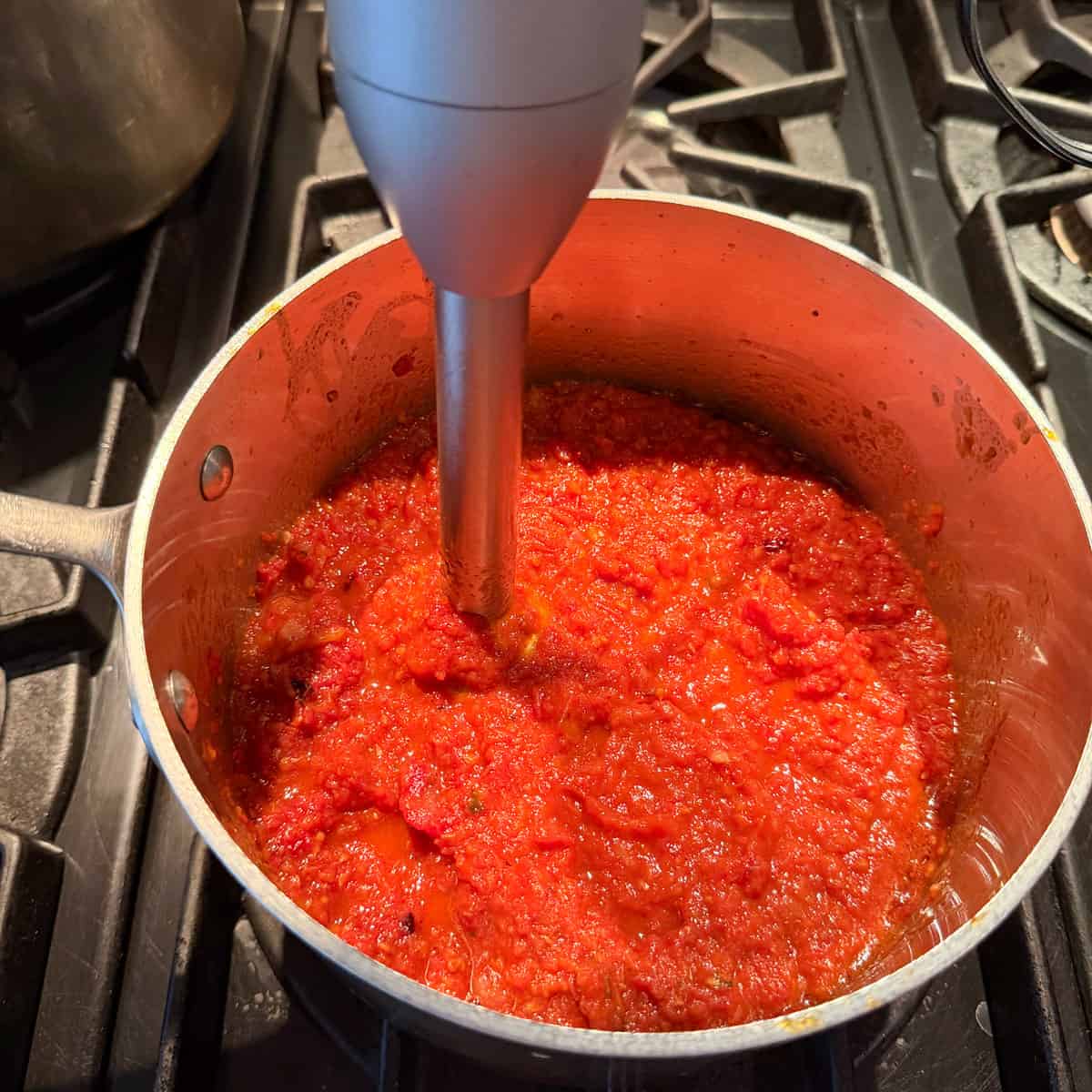 Roasted fresh tomato sauce being pureed with an immersion blender.