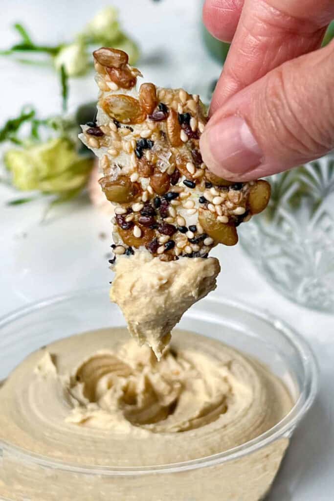 seed cracker being dipped into hummus