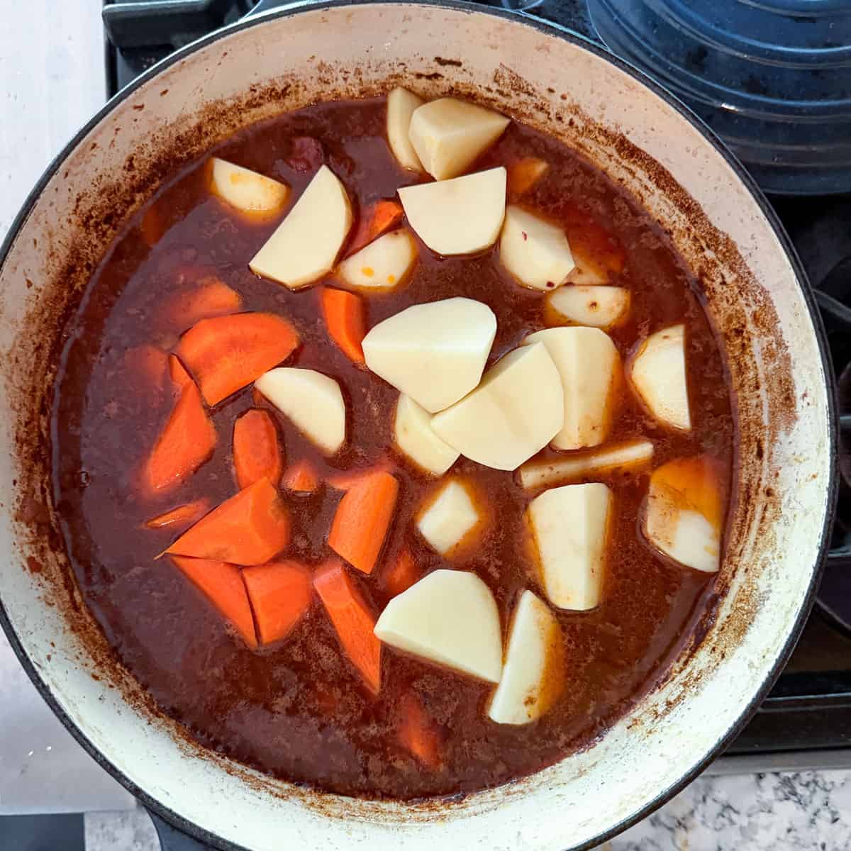 chunks of carrots and potatoes added to a pot of beef stew.