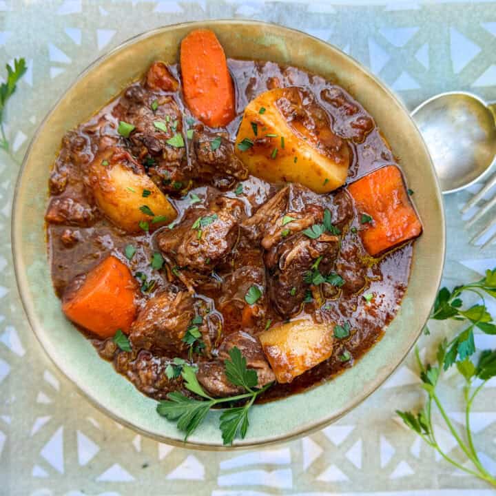 Beef stew with chunks of potatoes and carrots in a bowl with a sprig of parsley.